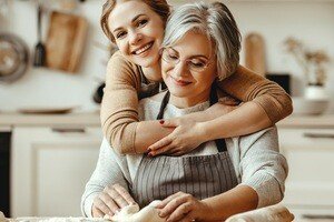 Altersarmut ist weiblich - junge Frau umarmt ältere Frau in der Küche