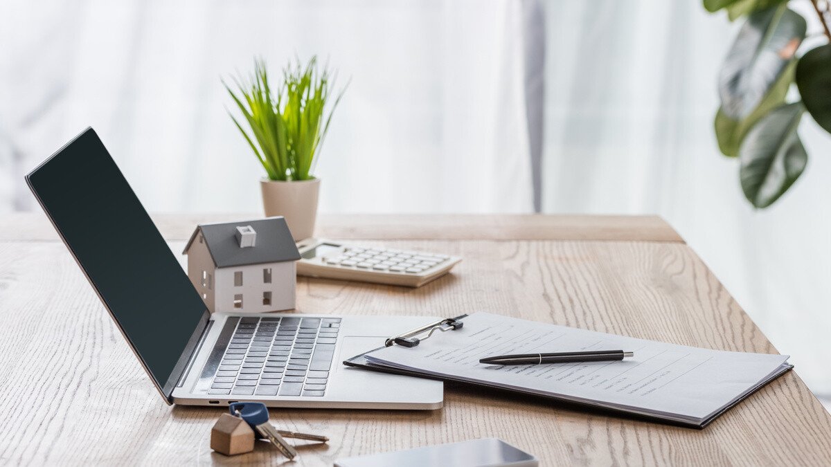Immobilien Teilverkauf - Schreibtisch mit Laptop, Notizen und Modellhaus