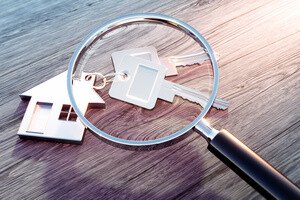 Immobilien Teilverkauf - Transparenz - Modellhaus als Schlüsselanhänger wird durch die Lupe betrachtet