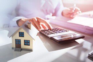Immobilienverrentung international - Schreibtisch mit Taschenrechner und Modellhaus