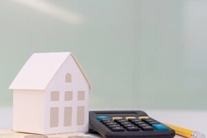 Liquidhome Teilverkauf - Modellhaus und Taschenrechner auf Schreibtisch