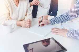 Notarkosten Hauskauf - 3 Leute sitzen über einem Vertrag am Schreibtisch