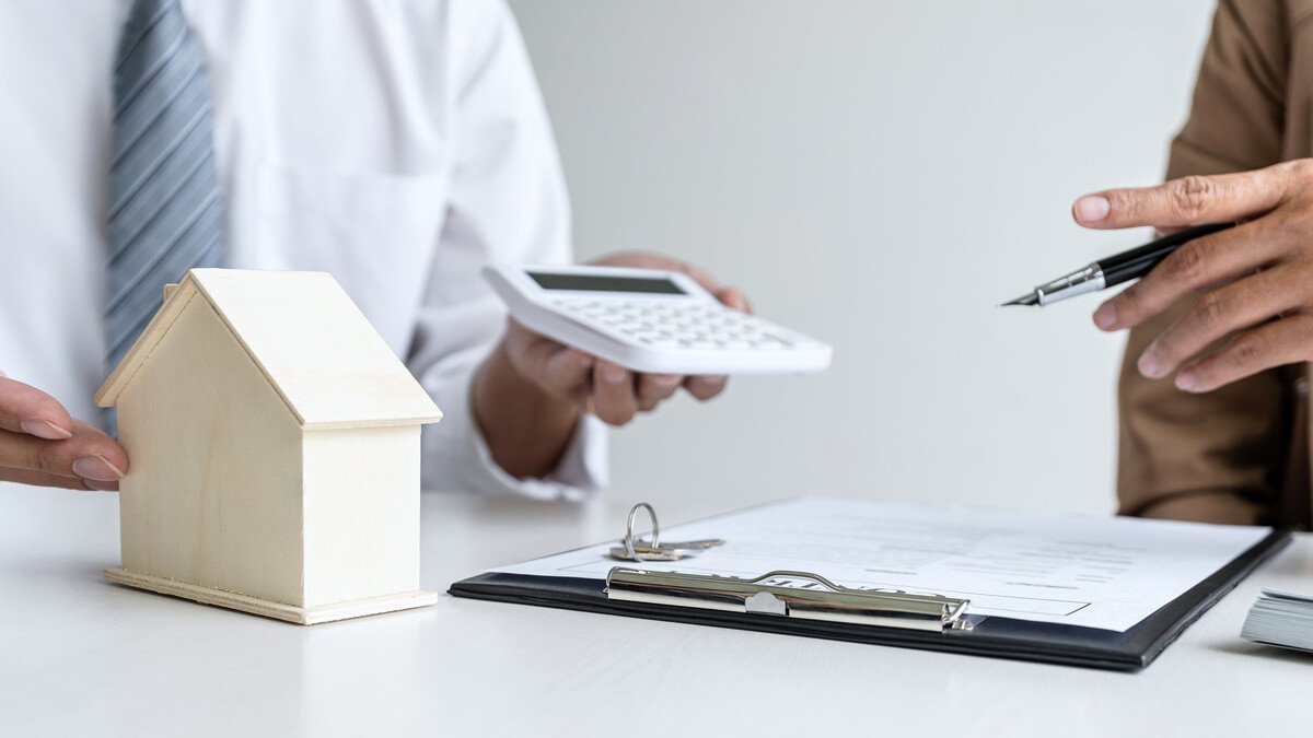 Kapitalanlage Pflegeimmobilien - Mann am Schreibtisch mit Taschenrechner und Modellhaus