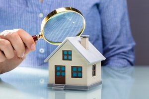 Änderung der Teilungserklärung - ein Mann betrachtet ein Modellhaus mit einer Lupe