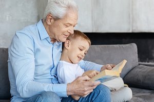 Erbengemeinschaft - Großvater mit Enkel lesen zusammen ein Buch auf der Couch