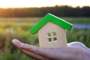 Erbteil verkaufen - Kleine Hausfigur liegt schützend in menschlicher Hand bei Sonnenlicht