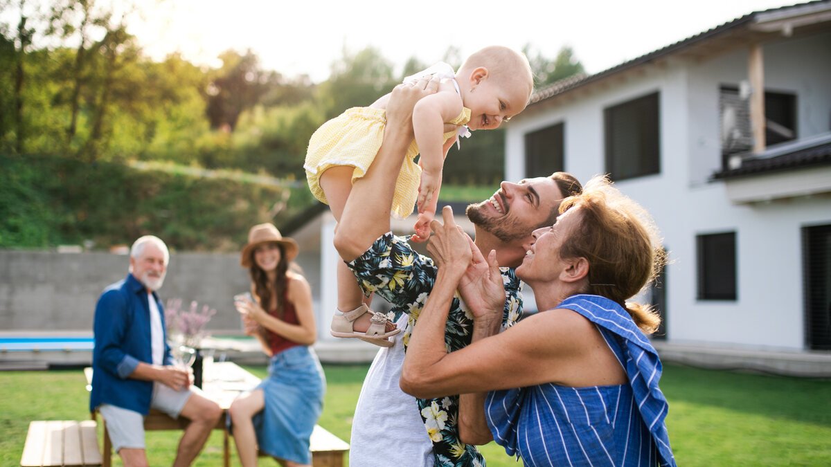 Familienheim erben - Mehrgenerationenfamilie mit Baby im Garten vor modernem Haus