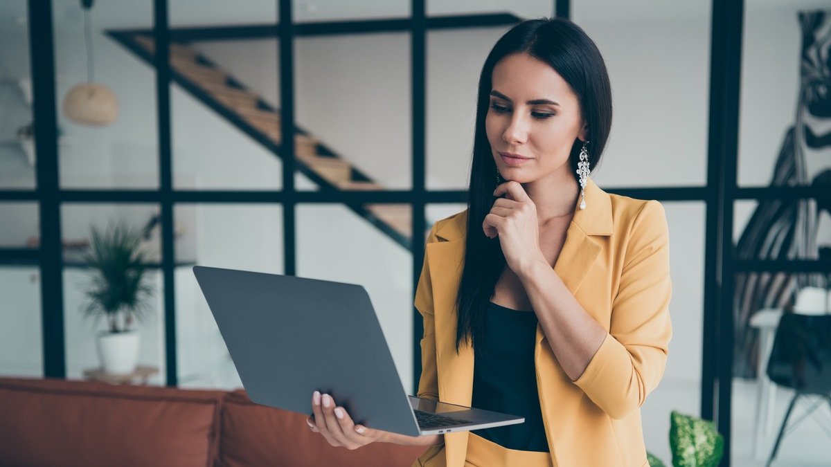 Frauen und Immobilien Frauen und Immobilien - Junge Frau steht nachdenklich mit Laptop im modernen Wohnraum