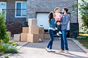 Frauen und Immobilien - Junge Familie mit Umzugskartons vor neuem Haus