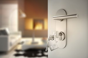 geerbte Immobilie verkaufen - Hausschlüssel steckt in Türschloss vor unscharfem Wohnraum