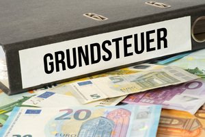 Immobilien als Erbschaftsvermögen - Euro Geldscheine und ein Ordner mit dem Grundsteuer Unterlagen