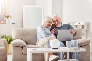 Immobilienteilverkauf - Seniorenpaar sitzt auf einem Sofa und schaut glücklich auf einen Laptop