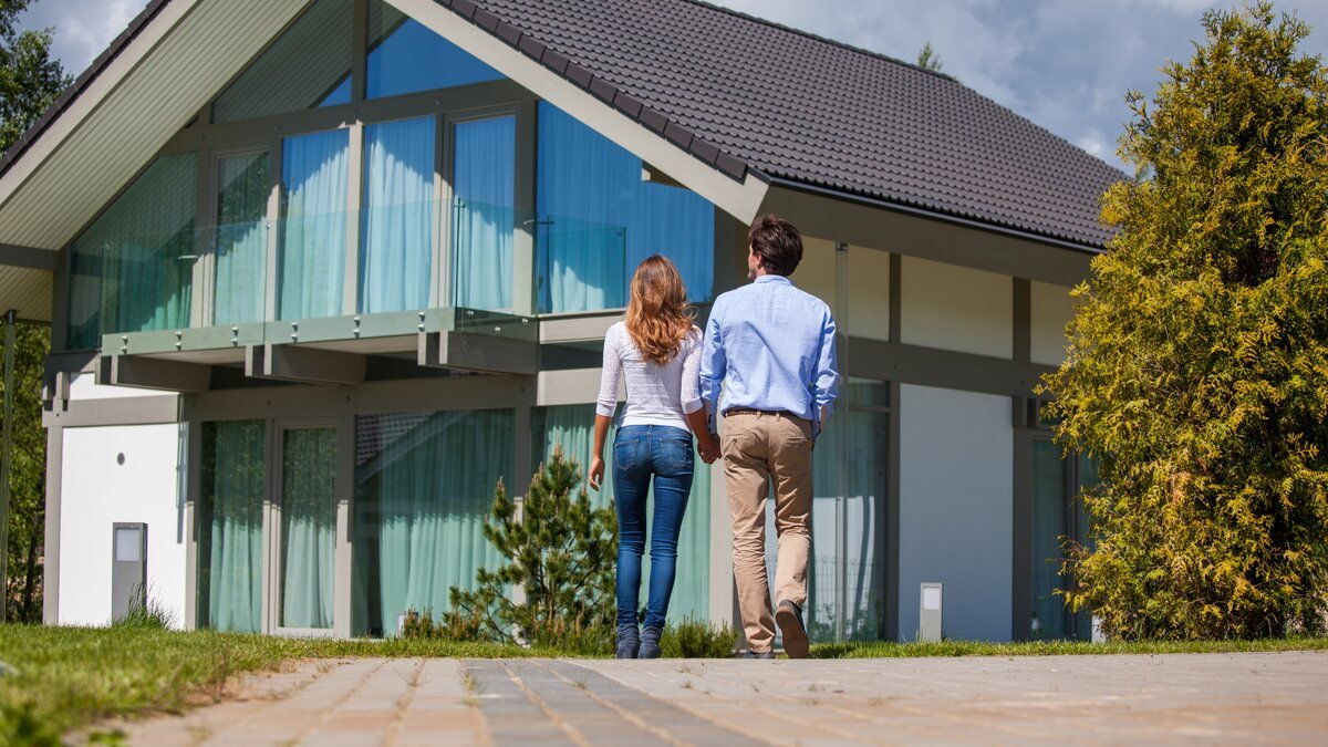 Immobilienteilverkauf - junges Paar steht vor einem modernen Wohnhaus mit Glasfront