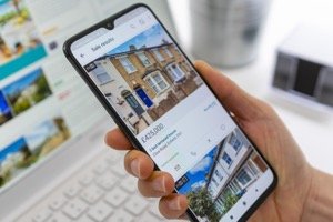 Mikroapartments kaufen - Smartphone zeigt Online-Immobilienangebot mit Hausfoto und Preis