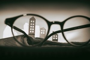 Mikroapartments kaufen - Papierhäuser auf Zeitung hinter großer Brille