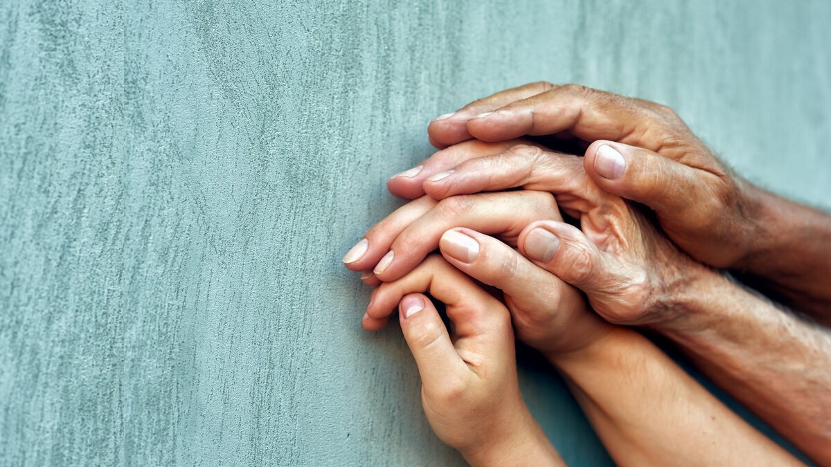 Hände verschiedener Generationen liegen schützend übereinander