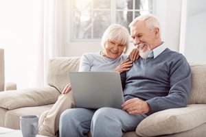 steigende_pflegekosten - Seniorenpaar nutzt Laptop gemeinsam auf dem Sofa